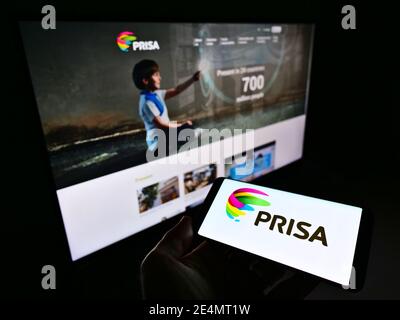 Person holding smartphone with business logo of Spanish media conglomerate Promotora de Informaciones S.A. (PRISA) on display. Focus on phone screen. Stock Photo