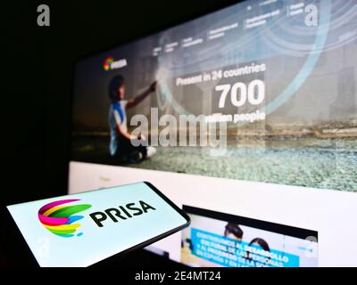 Person holding cellphone with company logo of Spanish media conglomerate Promotora de Informaciones S.A. (PRISA) on screen. Focus on phone display. Stock Photo