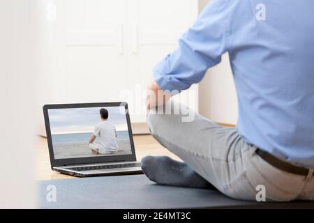 Businessman doing yoga or meditation exercise in front of laptop with man doing yoga on a beach - focus on the screen Stock Photo