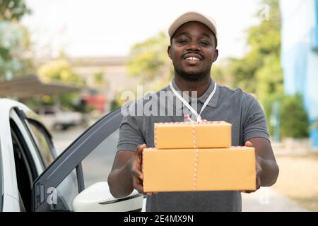 Smile african male postal delivery courier man in front of car delivering package Stock Photo