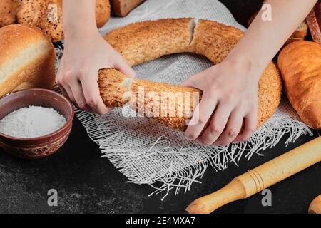 Woman holding bagel on dark table with various bread