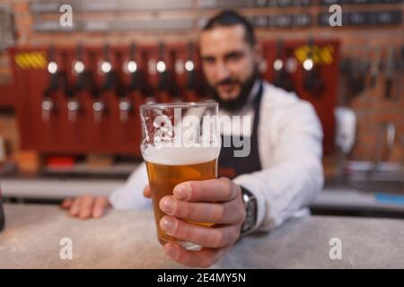 Bartender holding out beer glass to the camera, working at his pub Stock Photo