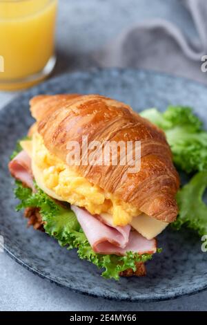 Breakfast croissant sandwich with scrambled eggs and ham on a blue plate, closeup view Stock Photo