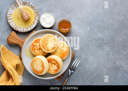 Syrniki, Cottage cheese or ricotta fritters served with honey and sour cream on grey concrete background, top view, copy space. Russian, Ukrainian cui Stock Photo