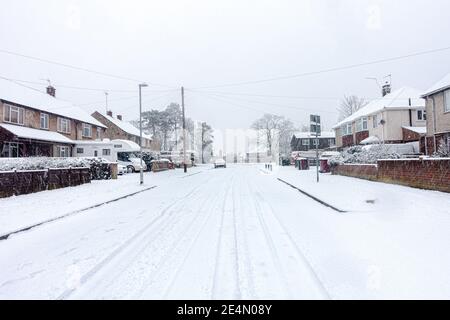 A residential road in Reading, Berkshire, UK is covered with snow. Car tracks lead into the distance. Stock Photo