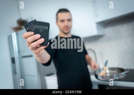 attractive young man holding protein bar in hand at modern kitchen Stock Photo