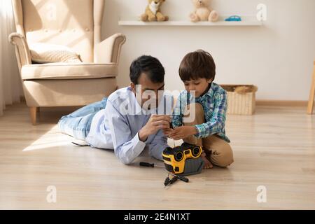 Caring hindu dad help little son to fix plastic truck Stock Photo