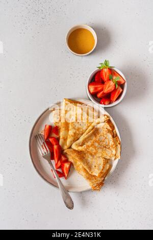 Traditional dish for holiday Maslenitsa. Thin crepes pancakes with honey, fresh strawberry and ingredients for making breakfast. Top view