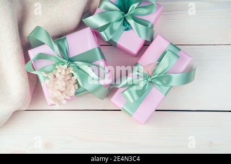 Three pink gift boxes with ribbons and a sweater on a white wooden background. Stock Photo