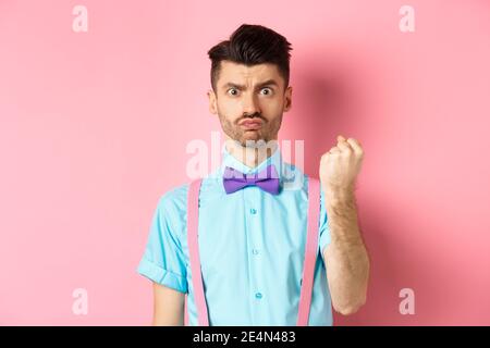 Silly man scolding someone, threaten person with fist, looking grumpy and disappointed, standing on pink background Stock Photo
