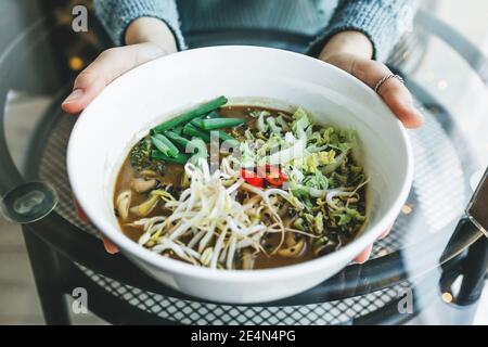 Close-up of a girl holding a plate with Ramen noodle soup in her hands. Asian traditional food. Stock Photo