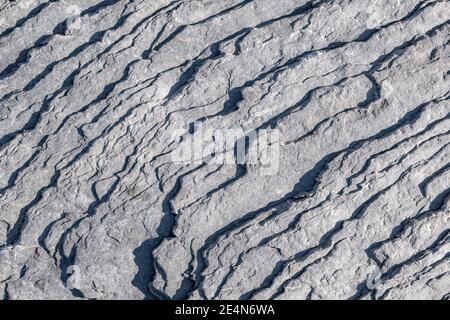 Layered rock on a sunny day. Harsh shadows at the edges of the layers. Rock is gray and worn from erosion. Looking down from above. Stock Photo