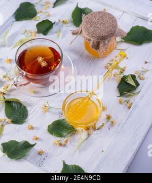 Linden Honey in Jar and bowl with a honey dipper on a white wooden table. Defocused branch of linden in the foreground. Stock Photo