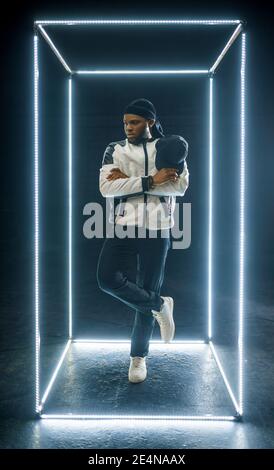 Rapper posing in illuminated cube, dark background. Hip-hop performer ...