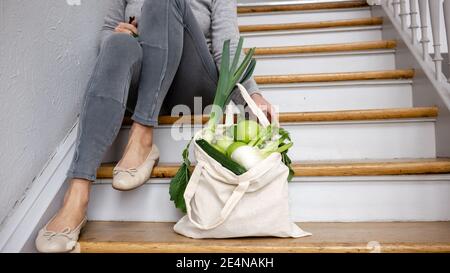 Woman with a plastic-free recycling groceries shopping bag and local  farm vegetables sits on the wooden staircase. Healthy vegan  sustainable life.