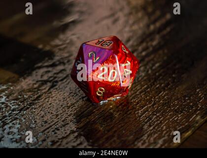 Close-up image of a marbled red 20 sided die on a wet wooden surface outside in the sunlight Stock Photo