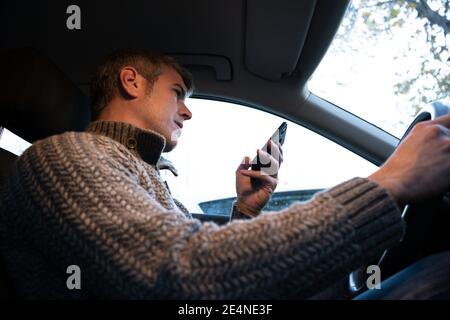 Young man using a smartphone while driving a car with one hand. Road safety Stock Photo