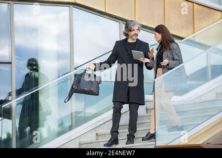 Confident mature businessman and his young subordinate with tablet discussing working points on the move while going downstairs Stock Photo