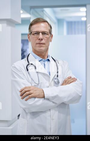 Confident old medical professional doctor standing arms crossed in hospital. Stock Photo