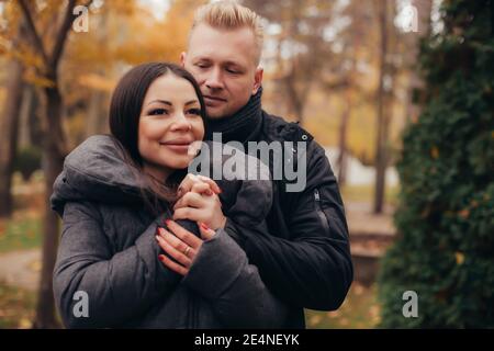 A man hugs and holds the hand of his girlfriend as she smiles in the cold weather in the autumn park. High quality photo Stock Photo