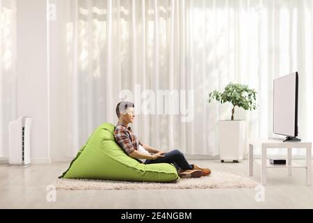 Profile shot of a guy sitting on a green bean bag chair and watching tv Stock Photo