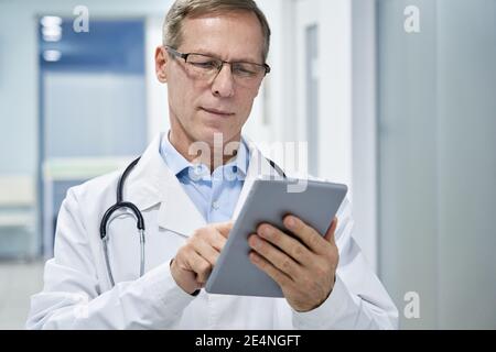Old doctor using digital tablet e health apps in hospital consulting online. Stock Photo