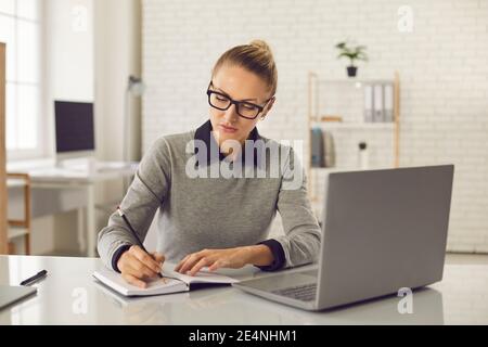 Focused woman taking online course, watching webinar and writing in her notebook Stock Photo