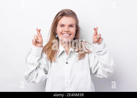 Photo of smiling young woman crossing fingers over white background. Stock Photo