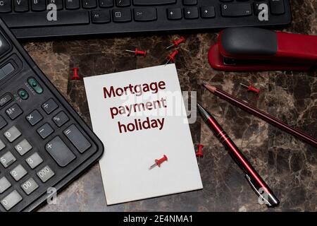 MORTGAGE PAYMENT HOLIDAY, text is written on a sheet of notepad lying on a marble writing table next to a pen and calculator. Stock Photo