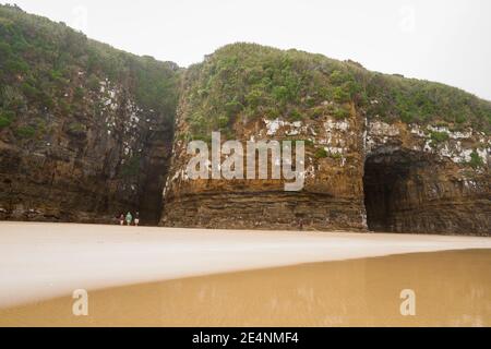 Catlins New Zealand - February 24 2015; Tourists dwarfed by huge Cathedral Caves on Waipati Beach rise 30 metres above the flat sand in Catlins area S Stock Photo