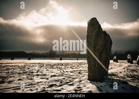 Weak winter sun breaks through snow clouds over a neolithic standing stone circle. Stock Photo