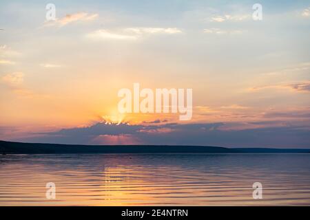Dramatic sunset over sea water with cloudy sky Golden colored nature background with calm water Stock Photo