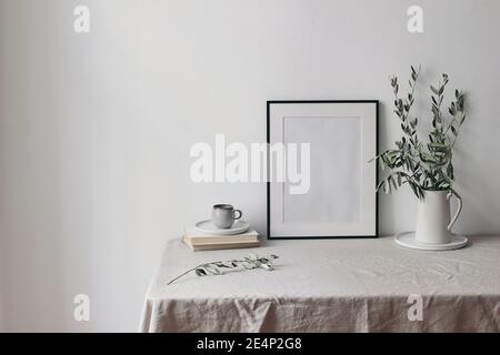 Spring, summer breakfast still life scene. Cup of coffee, books and empty black picture frame mockup. Beige linen tablecloth. Olive tree branches in Stock Photo