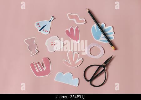 Paper cut abstract shapes, flowers and butterfly. Black old scissors and pencil on pink table background. Kids diy project, creativity and craft Stock Photo