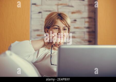 Beautiful middle aged woman using her laptop in the comfort of her living room. Stock Photo