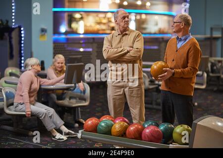 Portrait of two senior men playing bowling together with friends in background while enjoying active entertainment at bowling alley, copy space Stock Photo
