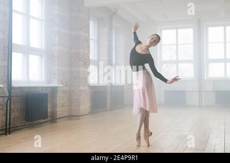 Young beautiful woman ballet dancer dressed in professional outfit pointe shoes and white tutu dancing in studio Stock Photo