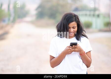 beautiful african woman using her phone outside on a bright sunny day, with blurred background Stock Photo