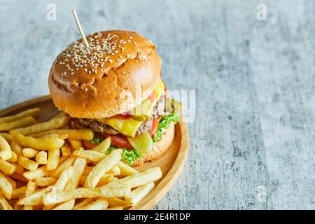 Big burger with fry potato in the wooden plate on the marble background Stock Photo