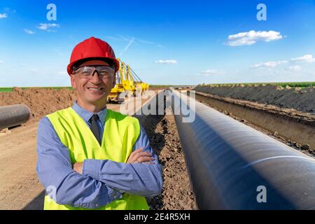 Happy Manager in Red Hardhat, Blue Shirt and Yellow Vest Looking at Camera. Portrait of Construction Foremen, Supervisor or Oil and Gas Engineer. Stock Photo