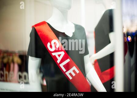 Close up red Sale Sign on mannequin In A Clothing Store. View through a glass of window case. Big discounts because of the store closing. Selective Stock Photo