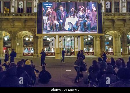 People sitting outside the Wiener Staatsoper or Vienna State Opera House view a performance for free on an outdoor screen Stock Photo