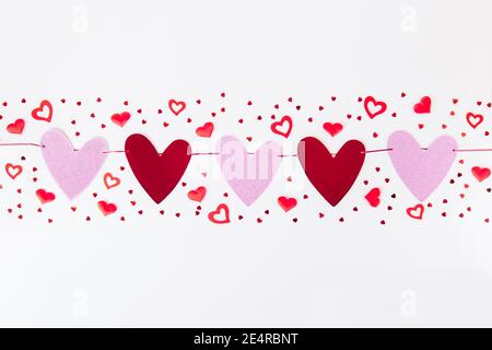 Paper red and pink hearts garland with other different hearts in a row on the white background. Valentine day background. Love concept. Selective Stock Photo