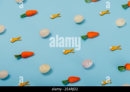 Easter pattern made of colored eggs, decorative carrots, and yellow bunny rabbits on pastel blue background. Minimal festive spring concept. Stock Photo