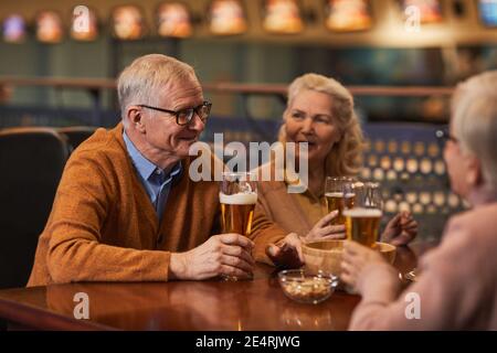 Portrait of smiling senior people drinking beer in bar while enjoying night out with friends, copy space Stock Photo