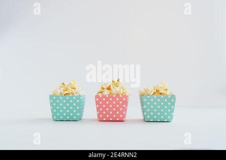 A row of blue and pink decorative small patterned paper boxes with popcorn on the white background. Child portion. Copy space, selective focus. Stock Photo
