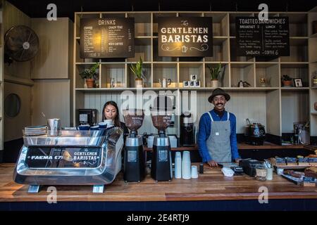 Coffee Business Concept - portrait of lady barista preparing and steaming milk for coffee order with her partner while standing at cafe. Stock Photo