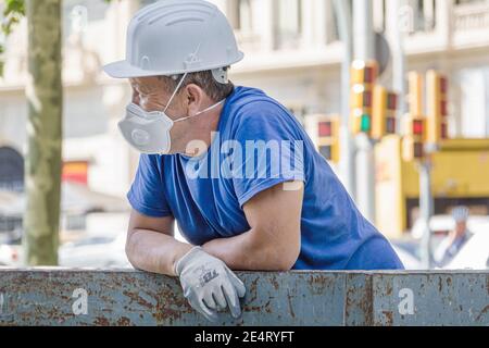 Spain Barcelona Catalonia Catalunya Avinguda Diagonal construction worker laborer taking break hard hat respirator mask gloves Hispanic man safety equ Stock Photo