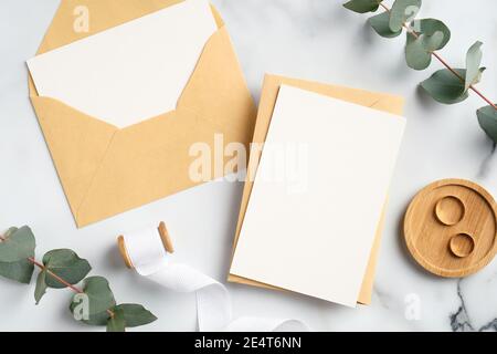 Wedding invitation cards, craft paper envelopes, ring, ribbon, eucalyptus branches on marble background. Bridal flat lay composition, top view. Rustic Stock Photo