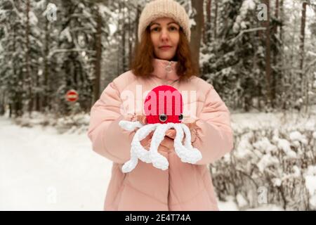 Beautiful girl with a knitted octopus toy in her hands on the street in winter, red color Stock Photo